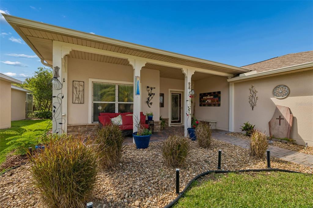 A covered front porch with a red sofa, potted plants, and stone landscaping — 184 VENTANA DR, POINCIANA, FL