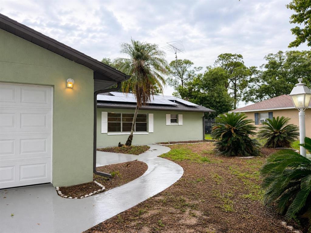 A light green house with a white garage door, solar panels, and a curved concrete walkway — 4401 MADERIA AVENUE, SEBRING, FL