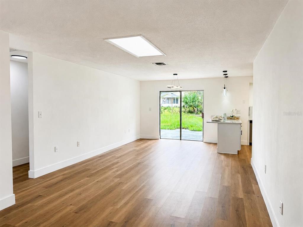 A bright living room features wood-look flooring, a sliding glass door, and a kitchen peninsula — 4401 MADERIA AVENUE, SEBRING, FL