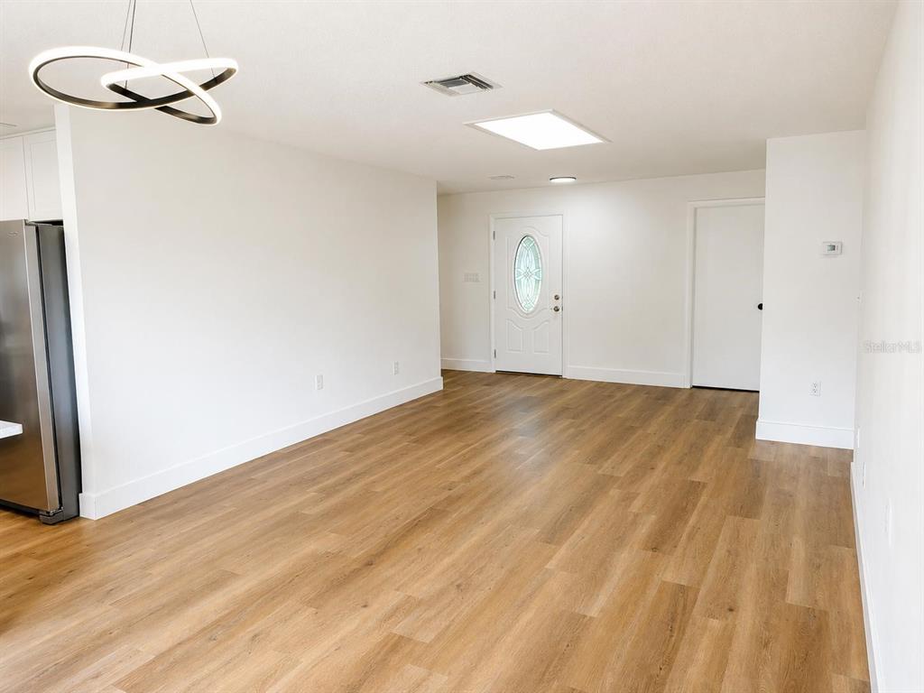 An open-concept living area features light wood-look flooring, a modern chandelier, and a white door — 4401 MADERIA AVENUE, SEBRING, FL