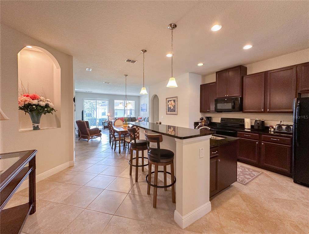 A kitchen with dark wood cabinets and a breakfast bar overlooks a dining area — 720 PARKMONT PLACE, WINTER GARDEN, FL