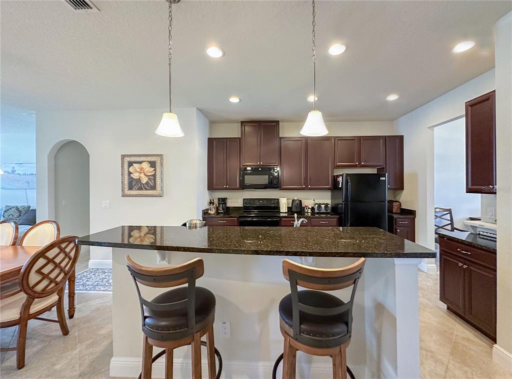 A kitchen features dark wood cabinets, a granite island with two stools, and black appliances — 720 PARKMONT PLACE, WINTER GARDEN, FL