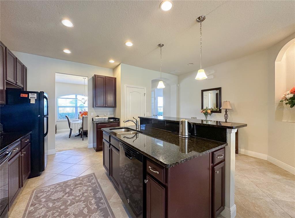 A kitchen features dark wood cabinets, granite countertops, a center island, and tile flooring — 720 PARKMONT PLACE, WINTER GARDEN, FL