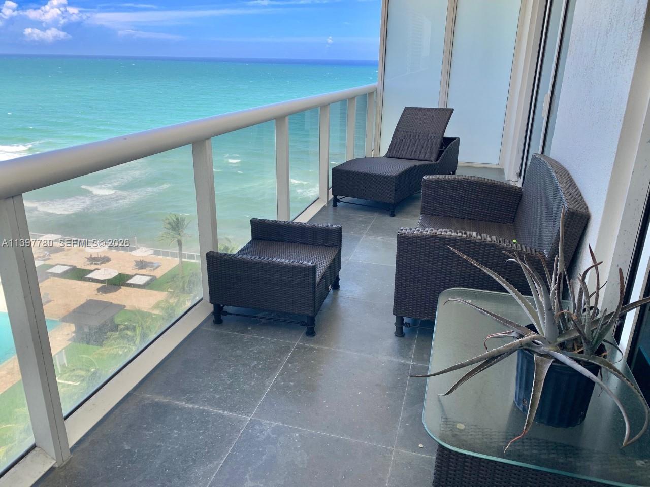A balcony with dark wicker furniture overlooks the ocean and a beach area below — 1830 S Ocean Dr # 1610, Hallandale Beach FL 33009, HALLANDALE BEACH, FL