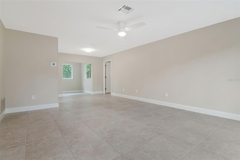 A spacious, neutral-toned room features large floor tiles, a ceiling fan, and an adjacent alcove — 2958 DUNDEE DRIVE, PALM HARBOR, FL