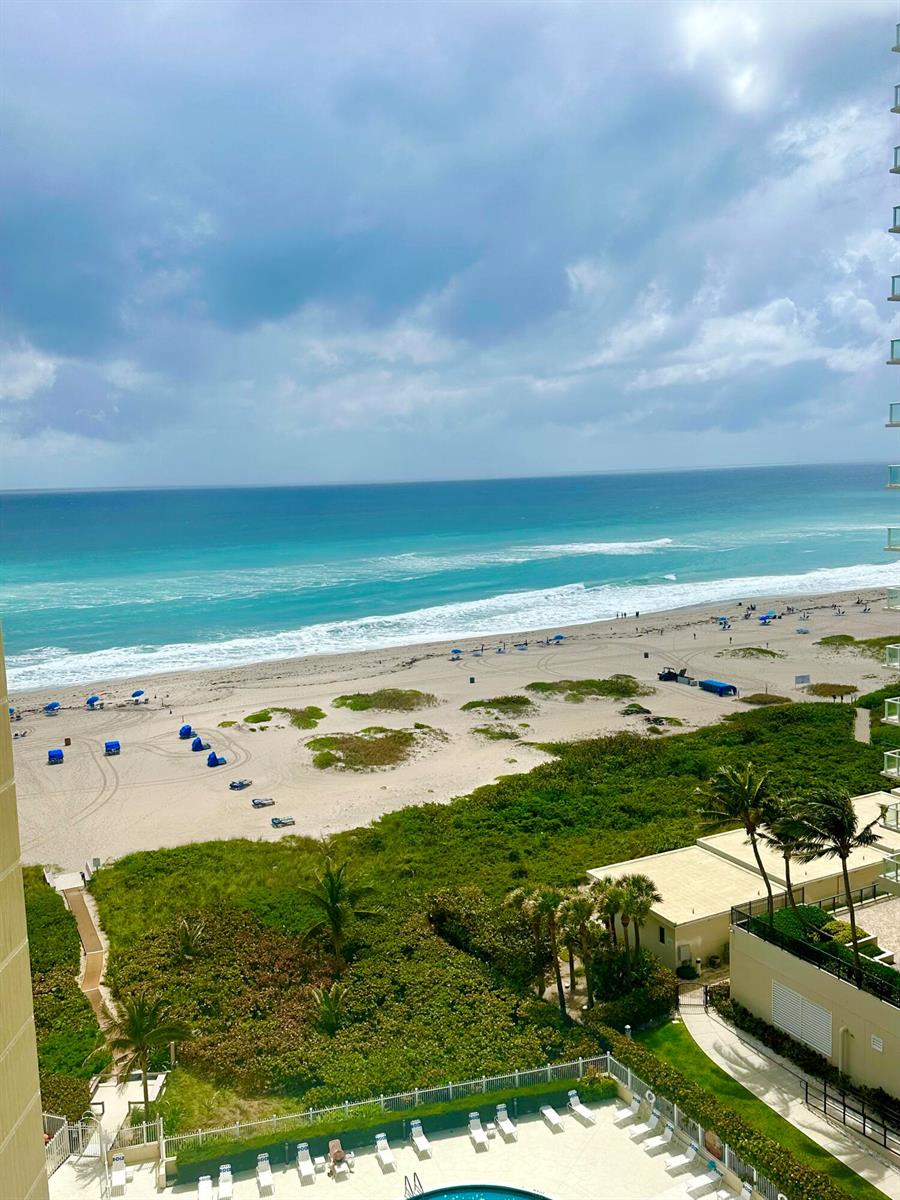 An elevated view of a sandy beach with blue umbrellas and the ocean beyond — 2800 N Ocean Drive # d, Singer Island FL 33404, SINGER ISLAND, FL