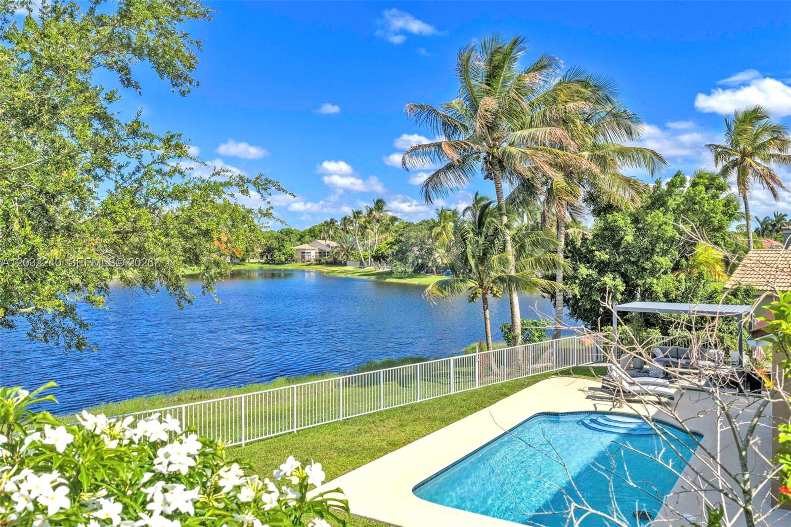 A backyard swimming pool overlooks a lake surrounded by palm trees and lush vegetation — 480 Cambridge Dr, Weston FL 33326, WESTON, FL