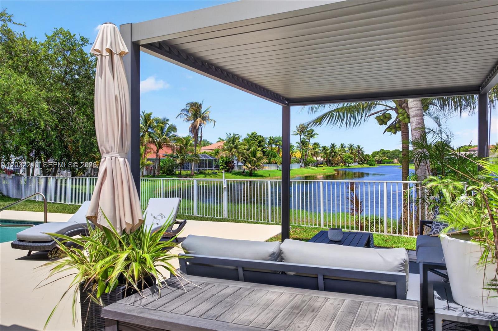 A patio with a pergola, outdoor furniture, and a view of a lake and palm trees — 480 Cambridge Dr, Weston FL 33326, WESTON, FL