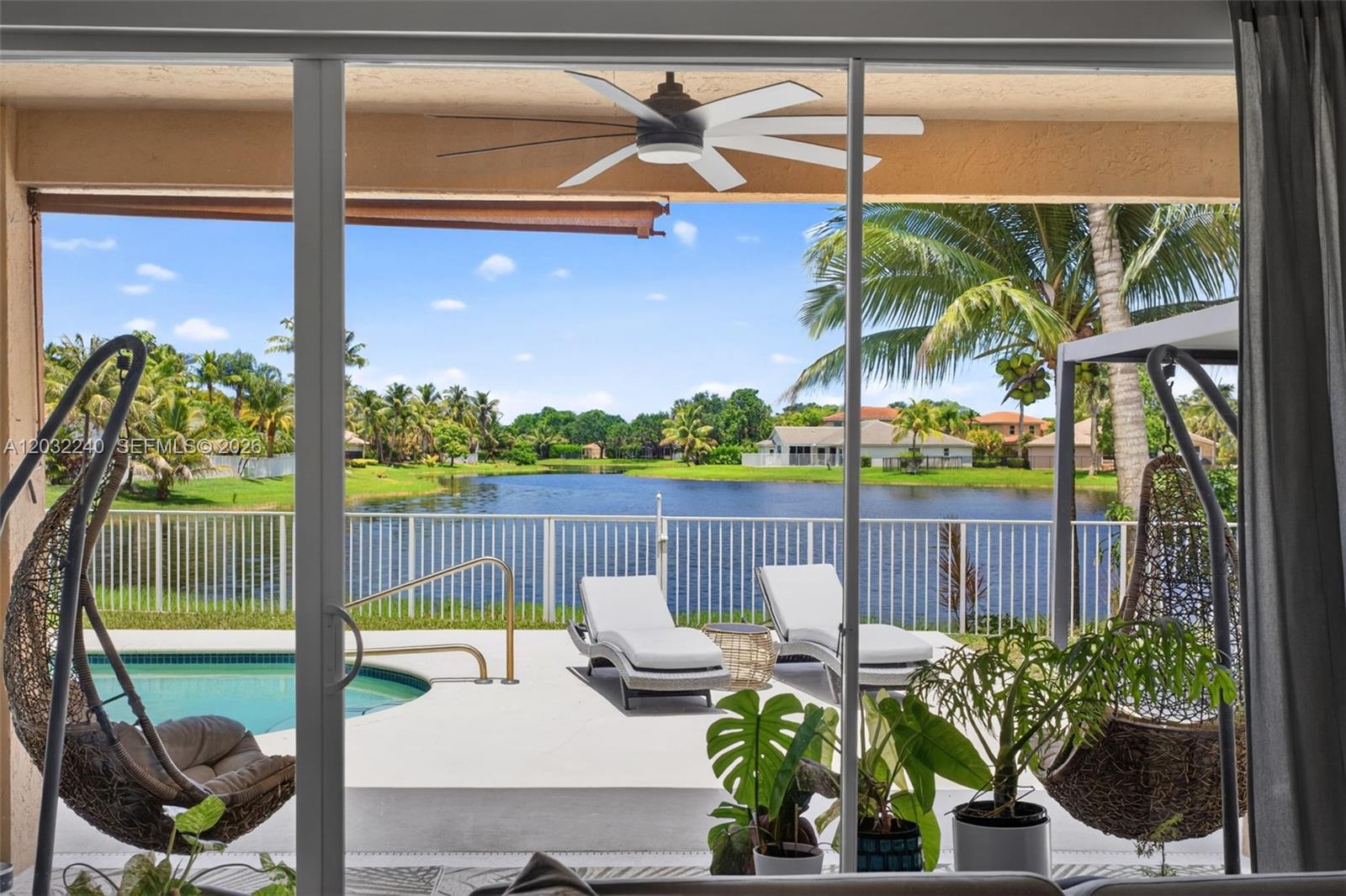 A view from a sliding glass door looking out onto a pool, patio, and lake — 480 Cambridge Dr, Weston FL 33326, WESTON, FL