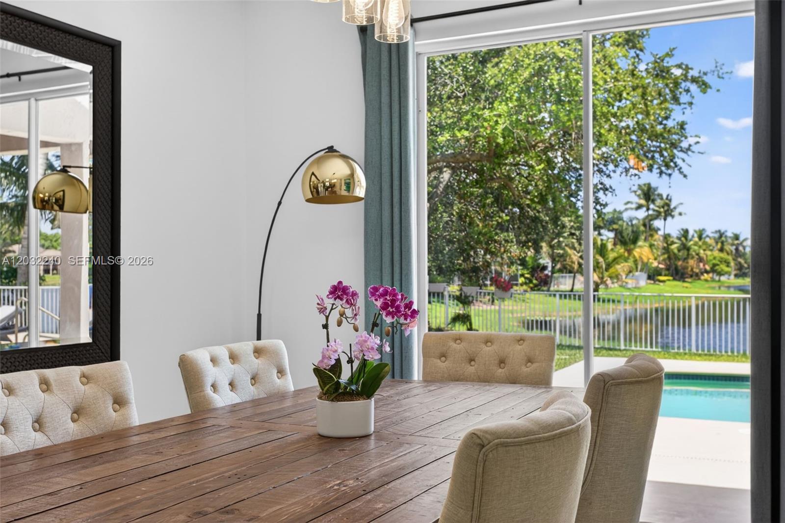 A dining room features a wooden table, tufted chairs, a floor lamp, and a pool view — 480 Cambridge Dr, Weston FL 33326, WESTON, FL