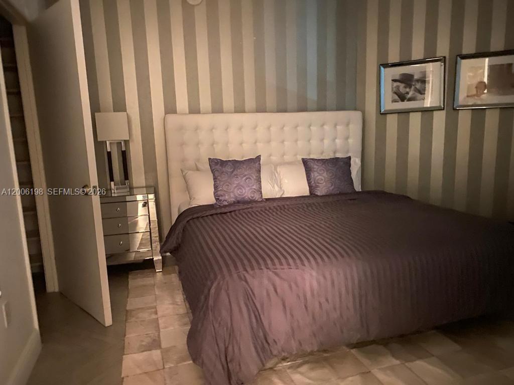 A bedroom features a tufted white headboard, striped wallpaper, and a mirrored nightstand — 1900 N Bayshore Dr # 2314, Miami FL 33132, MIAMI, FL