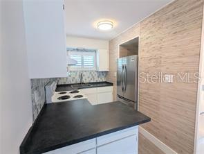 A kitchen features white cabinets, a black countertop, a stainless steel refrigerator, and wood-paneled walls — 2155 WOOD STREET UNIT A7, SARASOTA, FL