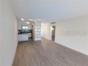 An open-concept living area with light wood-look flooring leads to a kitchen with white cabinets — 2155 WOOD STREET UNIT A7, SARASOTA, FL