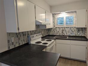 A kitchen features white cabinets, dark countertops, a tiled backsplash, and a white electric range — 2155 WOOD STREET UNIT A7, SARASOTA, FL