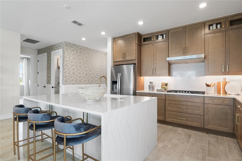A modern kitchen features a large white quartz island, wood cabinets, and blue velvet stools — 1838 PINECLIFF DRIVE, APOPKA, FL