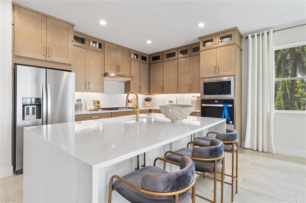 A modern kitchen features light wood cabinets, a white quartz island, and three velvet stools — 1838 PINECLIFF DRIVE, APOPKA, FL