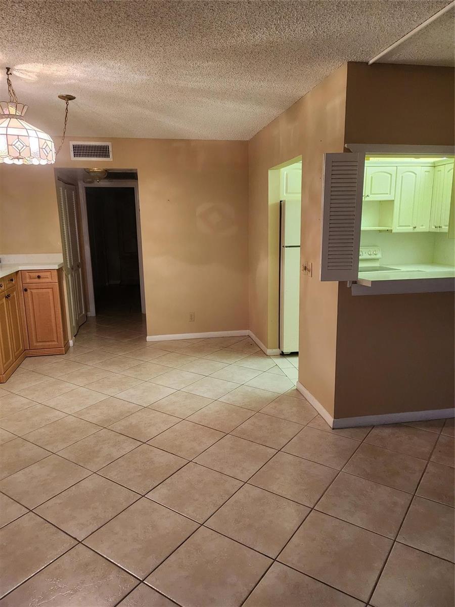 A kitchen and dining area featuring light-colored tile floors, wooden cabinets, and a pass-through window — 104 Westbury E, Deerfield Beach FL 33442, DEERFIELD BEACH, FL