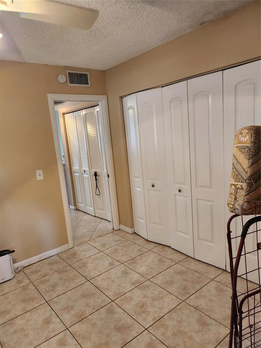 A room with beige walls, tiled flooring, and white bifold closet doors — 104 Westbury E, Deerfield Beach FL 33442, DEERFIELD BEACH, FL