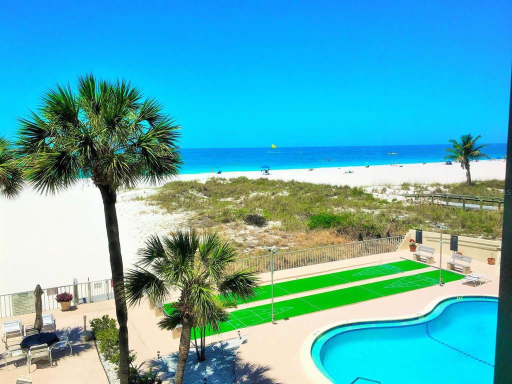 An elevated view of a beach, swimming pool, and shuffleboard courts from a balcony — 5000 GULF BOULEVARD UNIT 303, ST PETERSBURG, FL