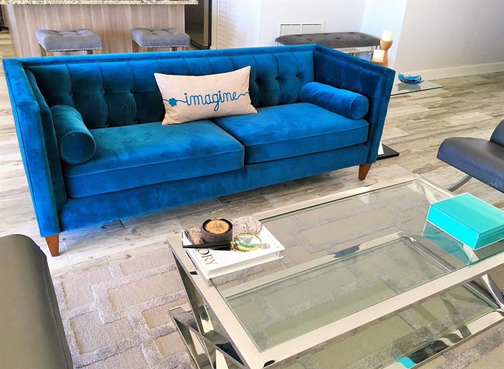 A blue tufted velvet sofa sits in a living room with a glass coffee table — 5000 GULF BOULEVARD UNIT 303, ST PETERSBURG, FL