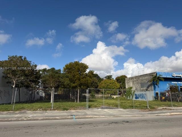 A vacant, fenced-in lot sits next to a commercial building under a blue sky — 102 NW 22nd Ave, Miami FL 33125, MIAMI, FL