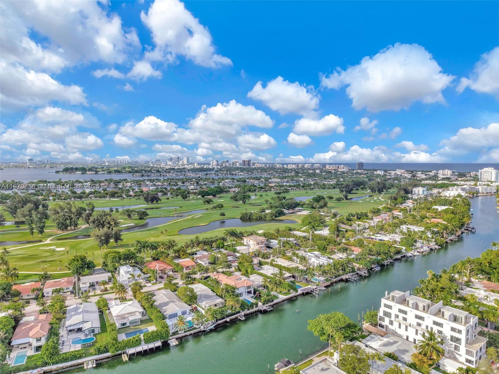 An aerial view shows waterfront homes, a golf course, and a distant city skyline — 1784 Marseille Dr, Miami Beach FL 33141, MIAMI BEACH, FL