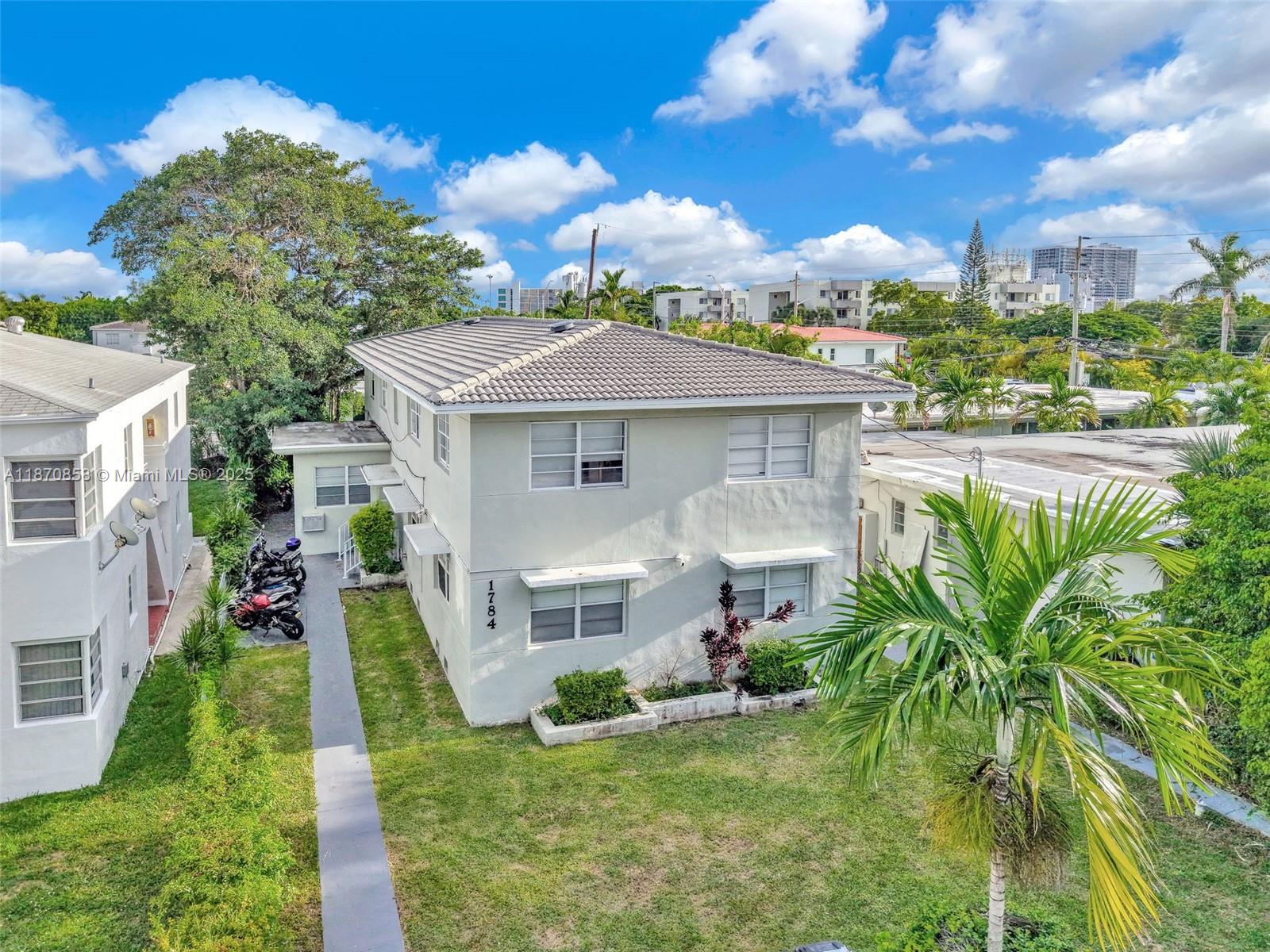 An exterior view of a two-story light-colored apartment building with a tiled roof — 1784 Marseille Dr, Miami Beach FL 33141, MIAMI BEACH, FL