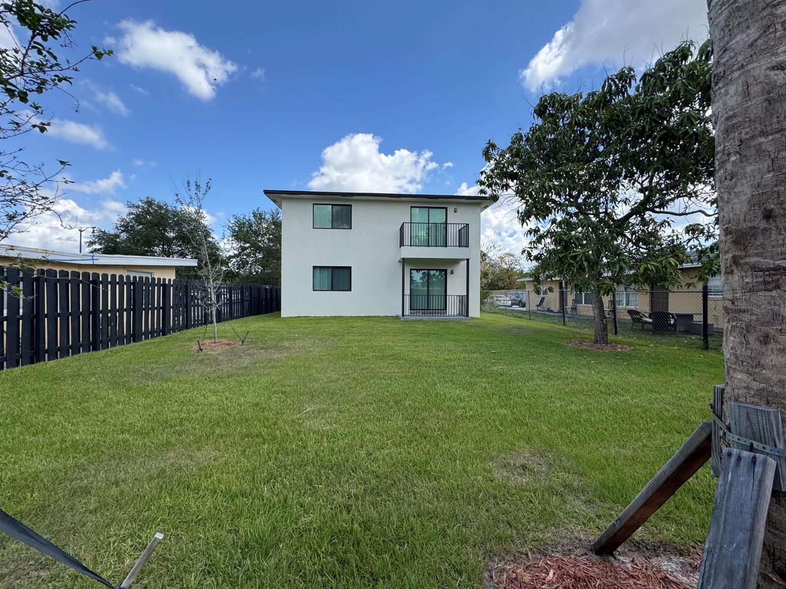 A two-story white house with a balcony stands in a grassy backyard with fencing — 400 NE 30th Street # 2, Pompano Beach FL 33064, POMPANO BEACH, FL