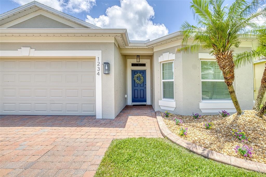 The exterior of a single-story house features a brick driveway, blue front door, and landscaping — 1234 CAP DIVILLE AVENUE, PORT ORANGE, FL