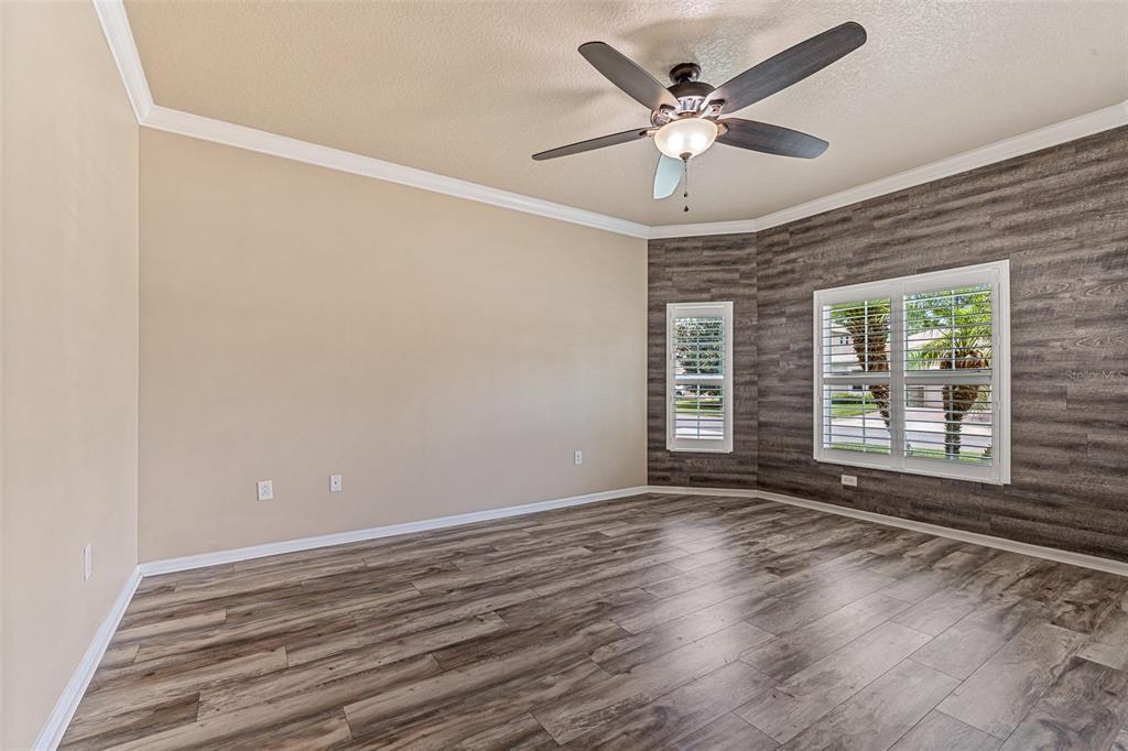 An empty room features wood-look flooring, a ceiling fan, and an accent wall with windows — 1234 CAP DIVILLE AVENUE, PORT ORANGE, FL