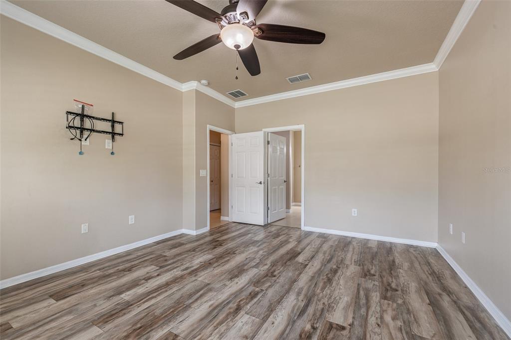 An empty bedroom features wood-look flooring, beige walls, a ceiling fan, and two open doorways — 1234 CAP DIVILLE AVENUE, PORT ORANGE, FL