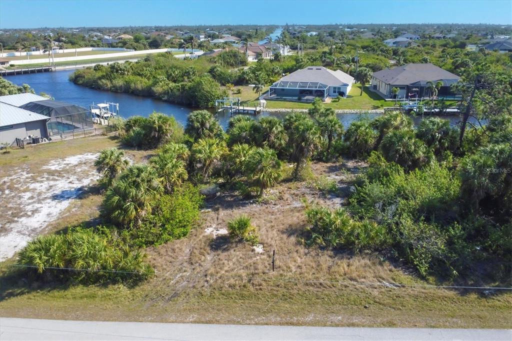 An aerial view of a vacant, brush-covered residential lot bordering a canal with nearby houses — 9984 WINNIPEG STREET, PORT CHARLOTTE, FL