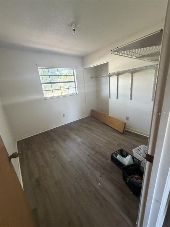 An empty bedroom features light-colored walls, wood-look flooring, a window, and open wall shelving — 3145 FLETCHER AVENUE, LAKELAND, FL
