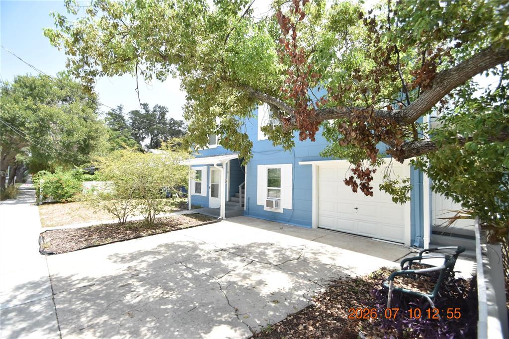 A blue two-story house features a concrete driveway, a single-car garage, and a large tree — 1156 SUNSET POINT ROAD UNIT A, CLEARWATER, FL