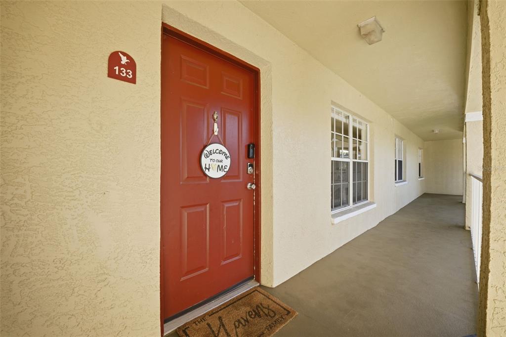 A red front door with a welcome sign and unit number 133 on a covered walkway — 2690 CORAL LANDINGS BOULEVARD UNIT 133, PALM HARBOR, FL