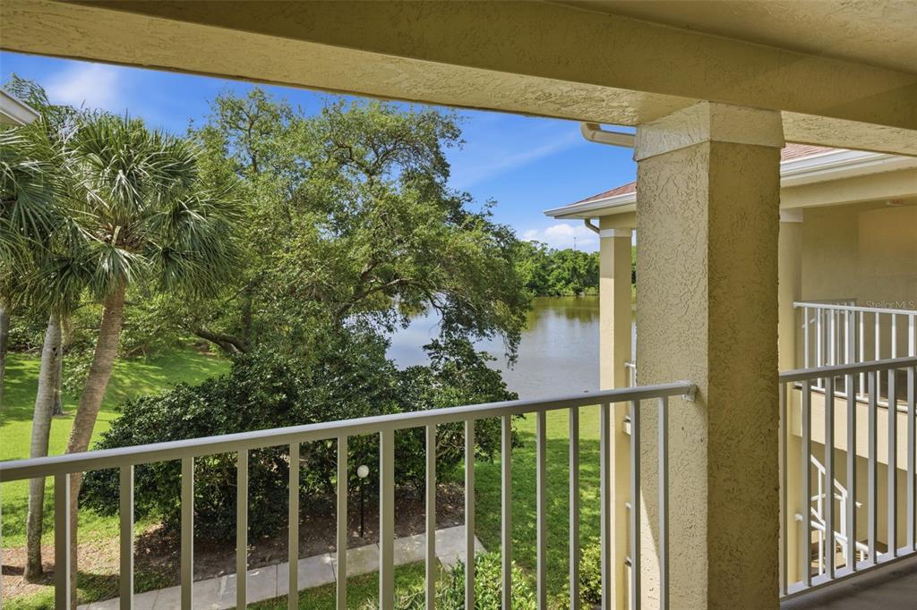 A view from a covered balcony overlooking a lake, trees, and a grassy lawn — 2690 CORAL LANDINGS BOULEVARD UNIT 133, PALM HARBOR, FL