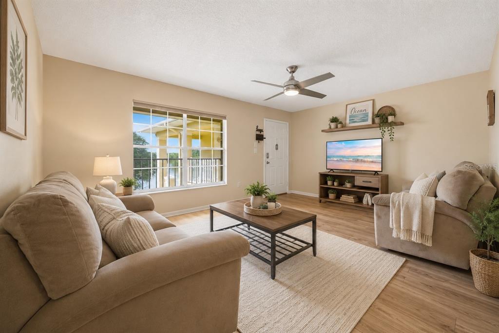 A living room features a beige sofa, wood-look flooring, a ceiling fan, and a television — 2690 CORAL LANDINGS BOULEVARD UNIT 133, PALM HARBOR, FL