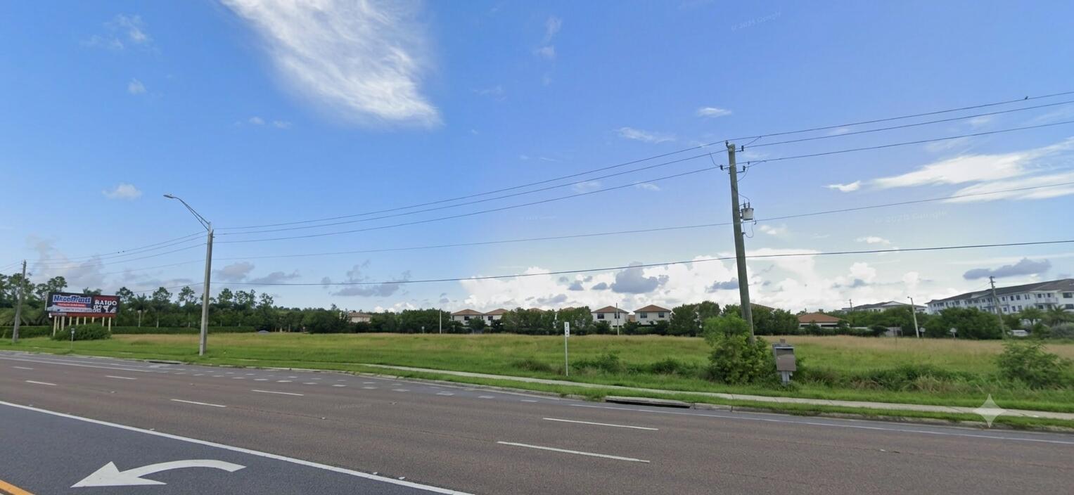 A large, flat, grassy vacant lot sits beside a multi-lane road under a blue sky — . Naples, Fl, Naples FL 34104, NAPLES, FL