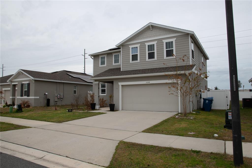 A two-story house with light gray siding and a two-car garage under a cloudy sky — 1054 HEIRLOOM DRIVE, HAINES CITY, FL