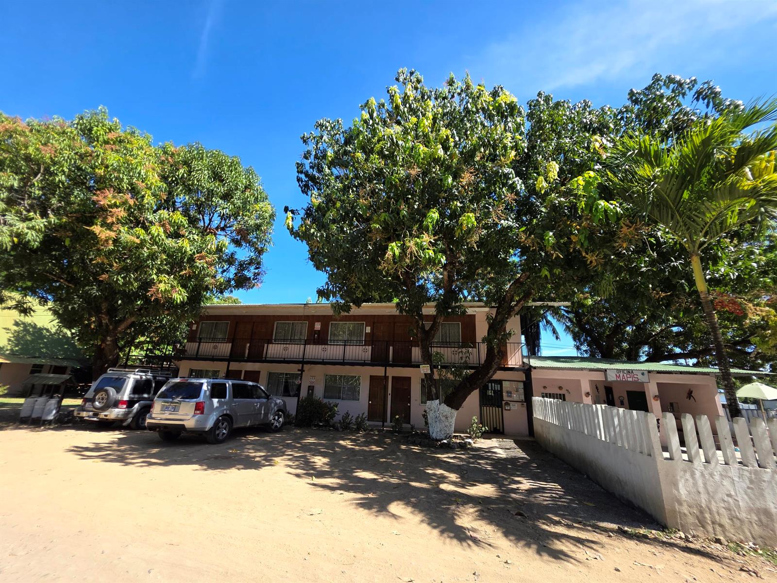 A two-story motel building with a dirt parking lot and large trees in front — 3.5km W From Paquera, 00000, FL