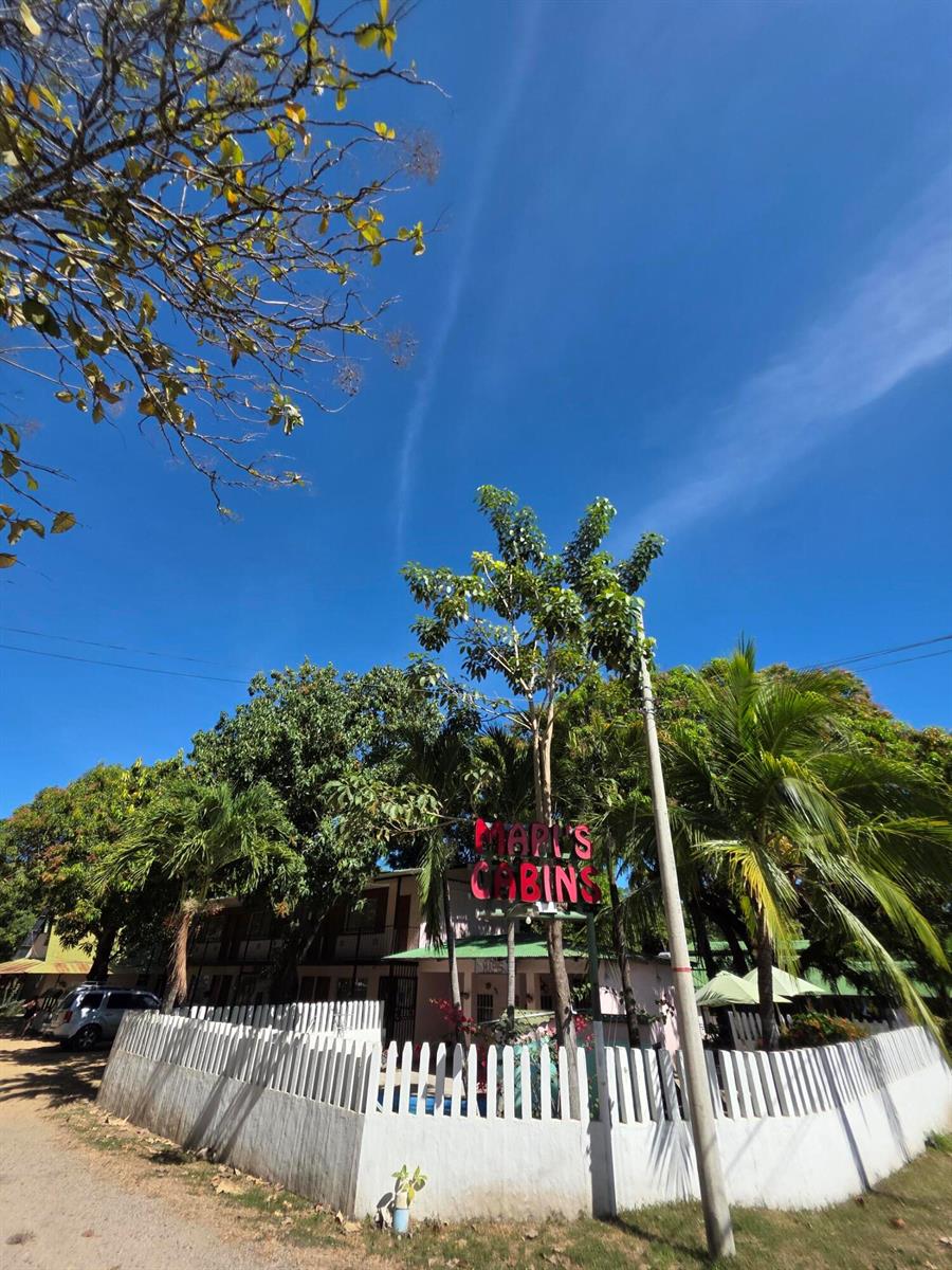 A white picket fence surrounds a property with a sign reading Earl's Cabins — 3.5km W From Paquera, 00000, FL