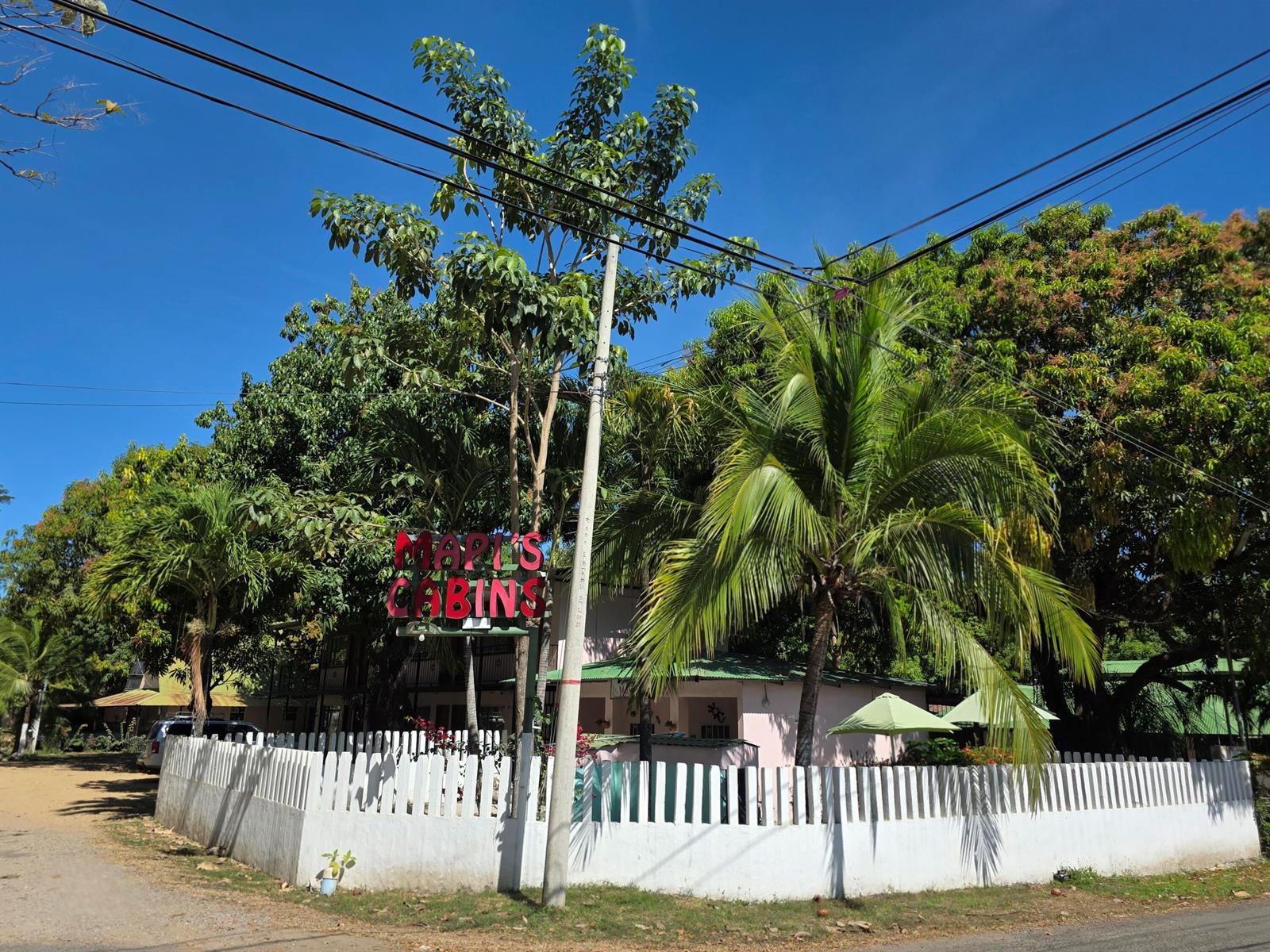 A white picket fence surrounds a pink building with a sign reading Maples Cabins — 3.5km W From Paquera, 00000, FL