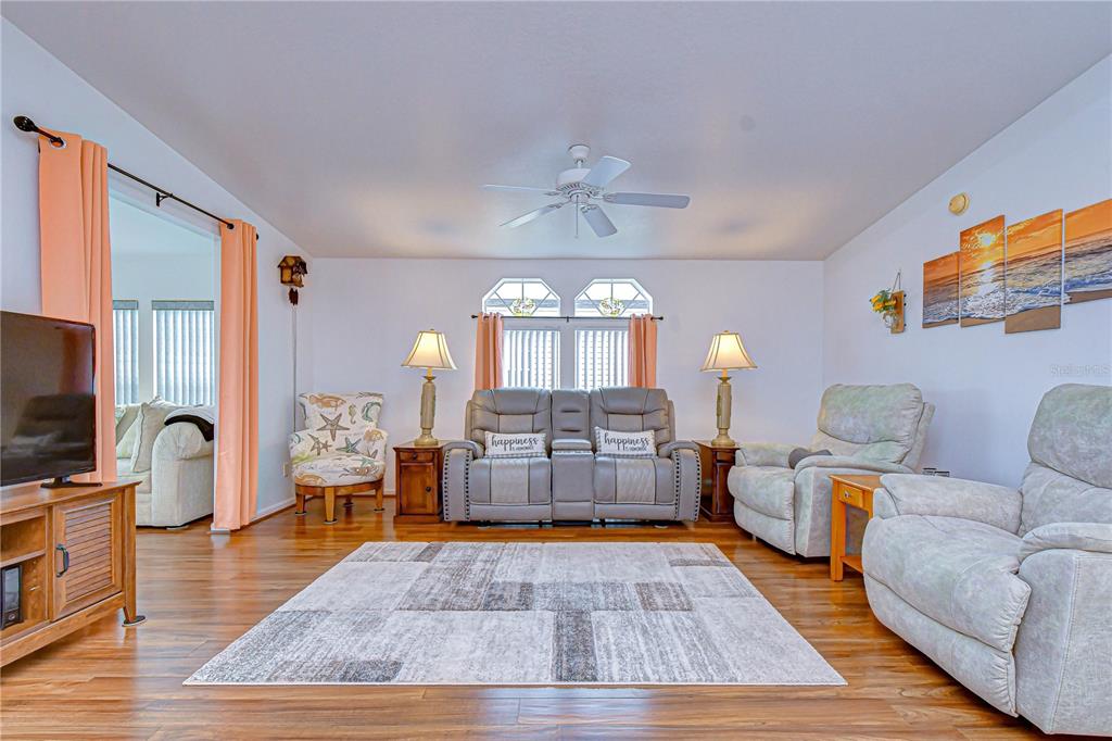 A living room features light wood flooring, a gray loveseat, two recliners, and a patterned rug — 37232 NEUKOM AVENUE, ZEPHYRHILLS, FL