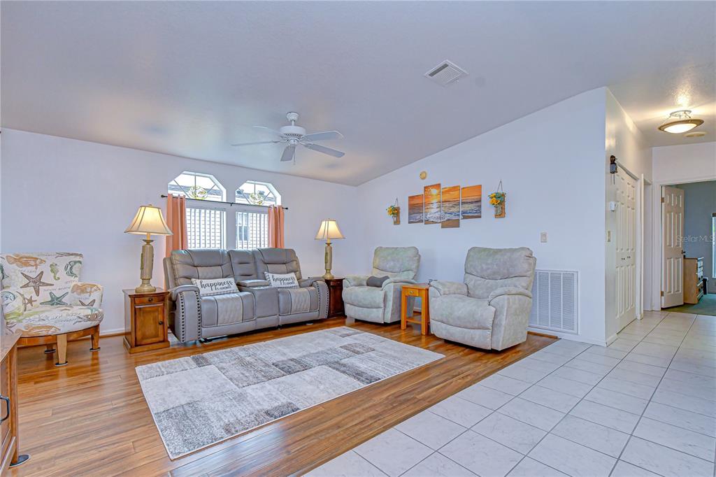A living room features wood-look flooring, a gray sofa, two recliners, and a patterned armchair — 37232 NEUKOM AVENUE, ZEPHYRHILLS, FL