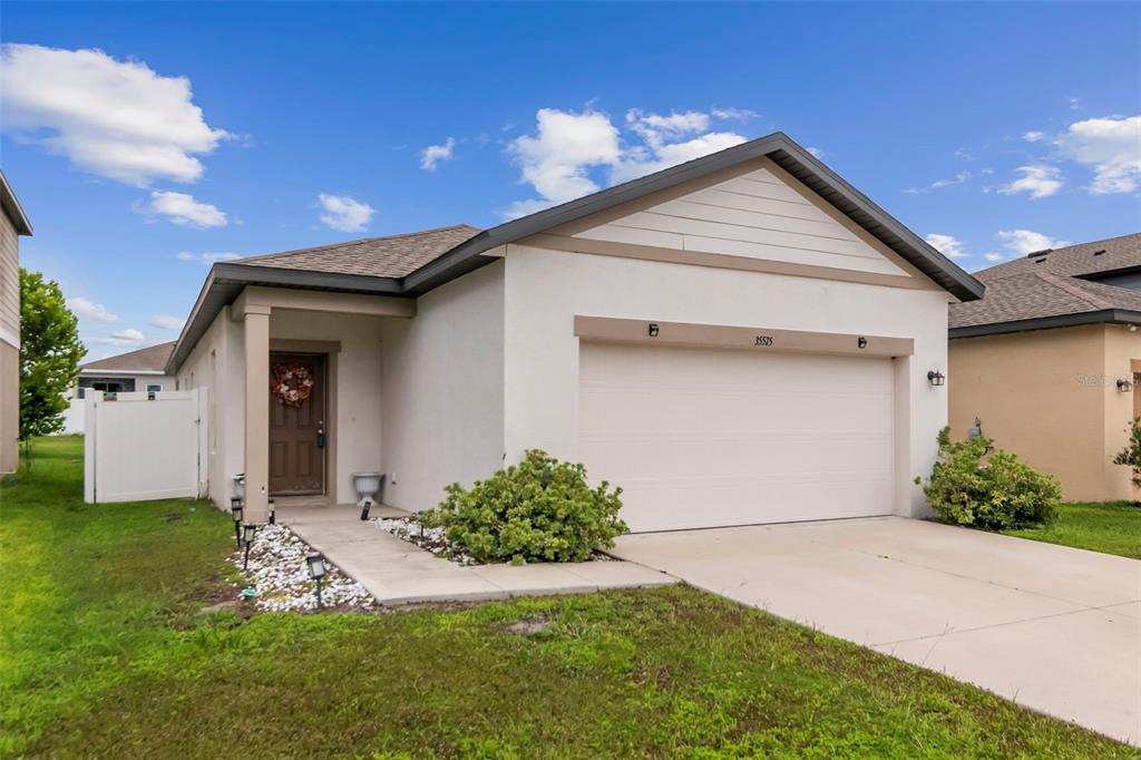 A single-story suburban house with a white stucco facade, a two-car garage, and a driveway — 35575 BUTTONWEED TRL, ZEPHYRHILLS, FL