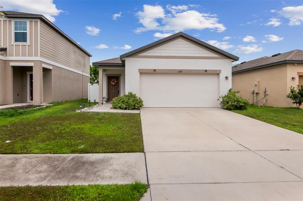 An open-concept kitchen with white cabinets and an island overlooks a carpeted living area — 35575 BUTTONWEED TRL, ZEPHYRHILLS, FL