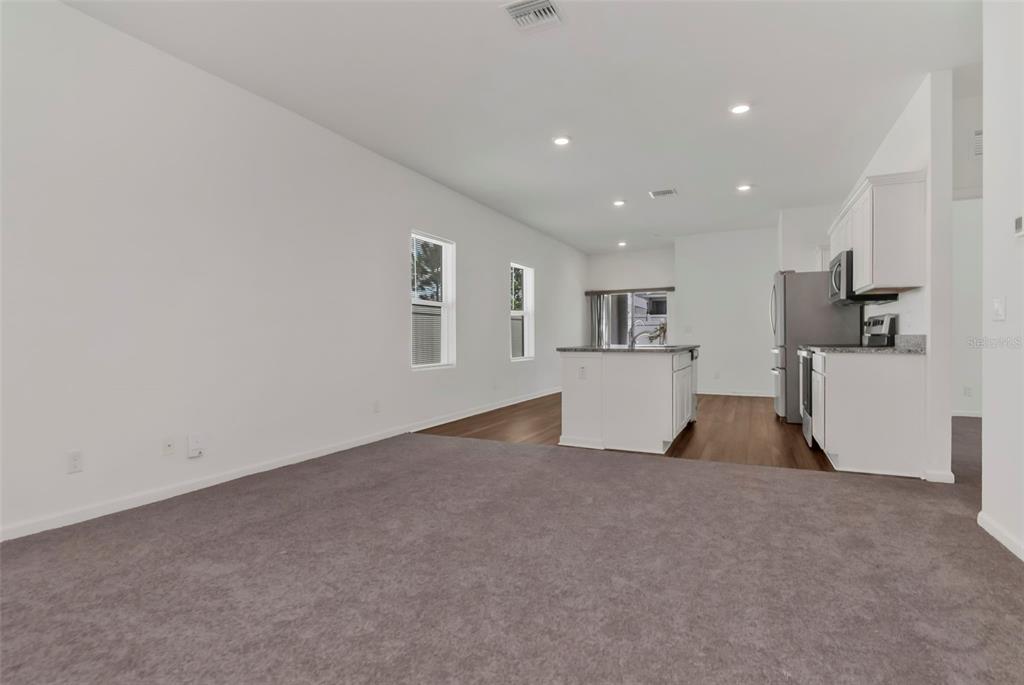 An empty room features beige carpet, white walls, a white door, and a window — 35575 BUTTONWEED TRL, ZEPHYRHILLS, FL