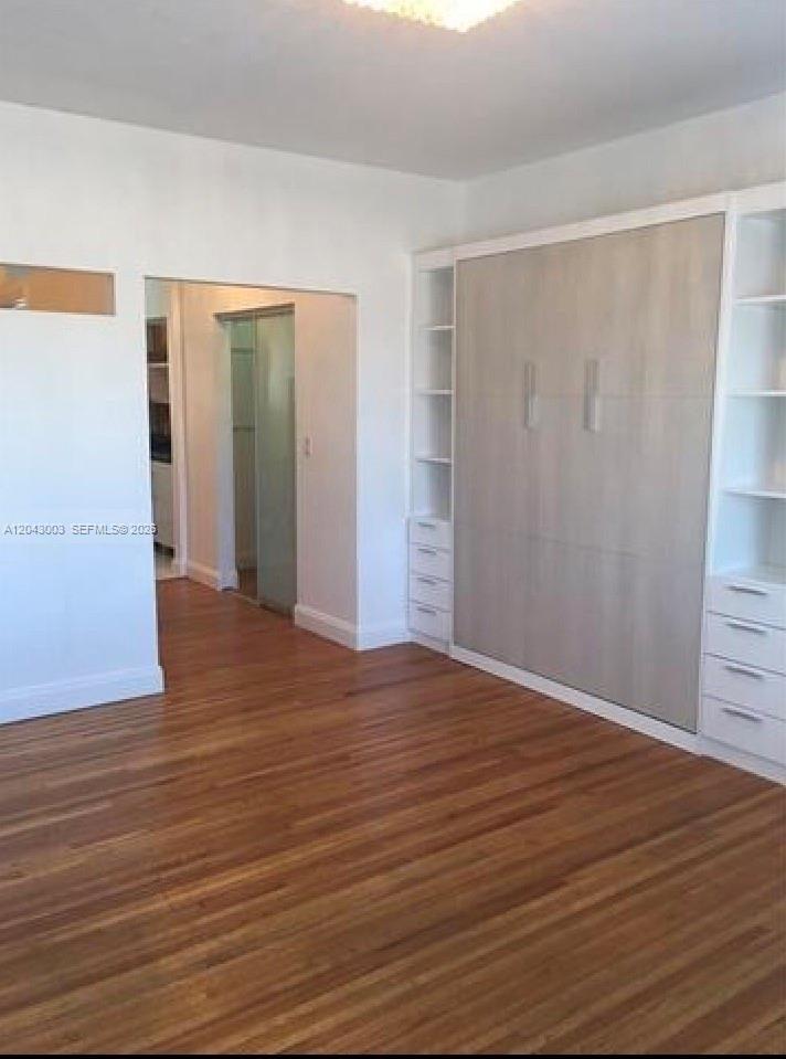 A room with hardwood floors features a large built-in wall unit and a doorway — 503 74th St # B3, Miami Beach FL 33141, MIAMI BEACH, FL