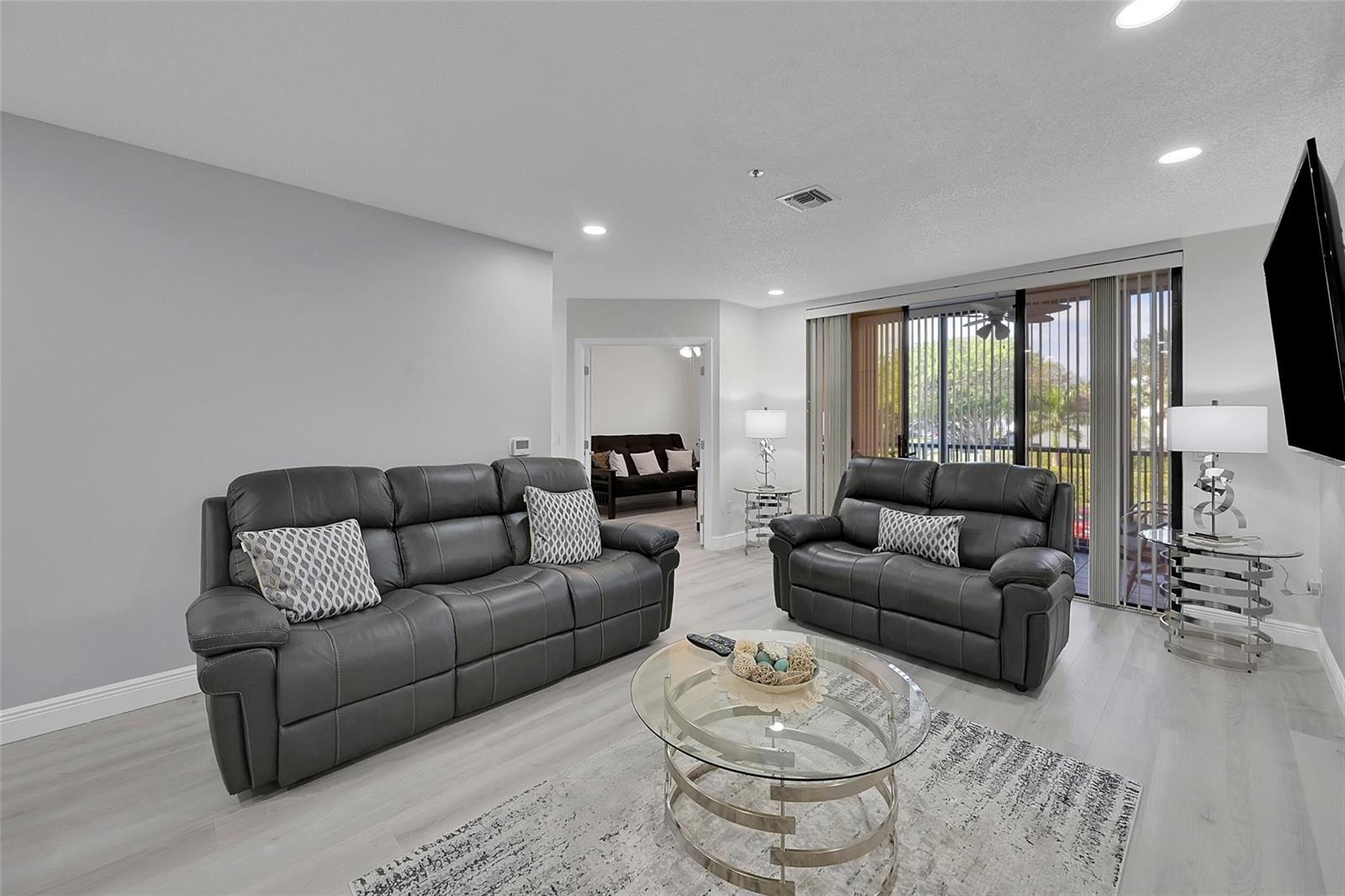 A living room features gray leather sofas, a glass coffee table, and a sliding glass door — 5133 Brisata Circle # P, Boynton Beach FL 33437, BOYNTON BEACH, FL