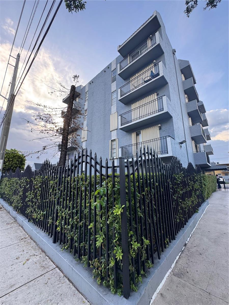 A low-angle view of a multi-story blue apartment building behind a black metal fence — 1933 SW 7th St # 504, Miami FL 33135, MIAMI, FL